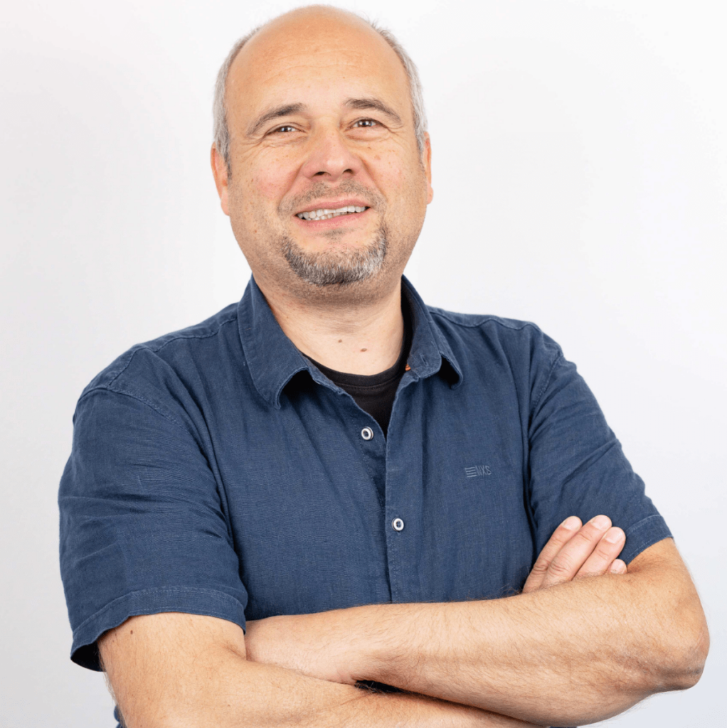 Gerwin Withaar: Porträtfoto eines Mannes mittleren Alters mit kurzem, grauem Haaransatz und einem dunkelblauen Hemd. Auch er lächelt leicht und hat die Arme vor der Brust verschränkt. Seine Position ist ebenfalls Projektleitung.