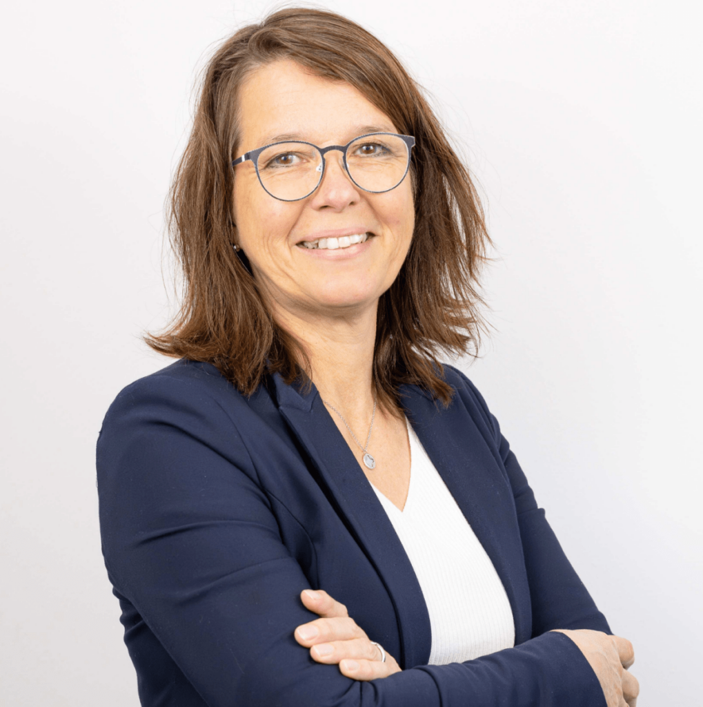 Sigrid Zweers: Porträtfoto einer Frau mittleren Alters mit braunem, schulterlangem Haar und Brille. Sie trägt ein dunkelblaues Sakko über einem weißen Oberteil, lächelt dezent und hat die Arme vor der Brust verschränkt. Ihre Rolle ist Finanzbuchhaltung.